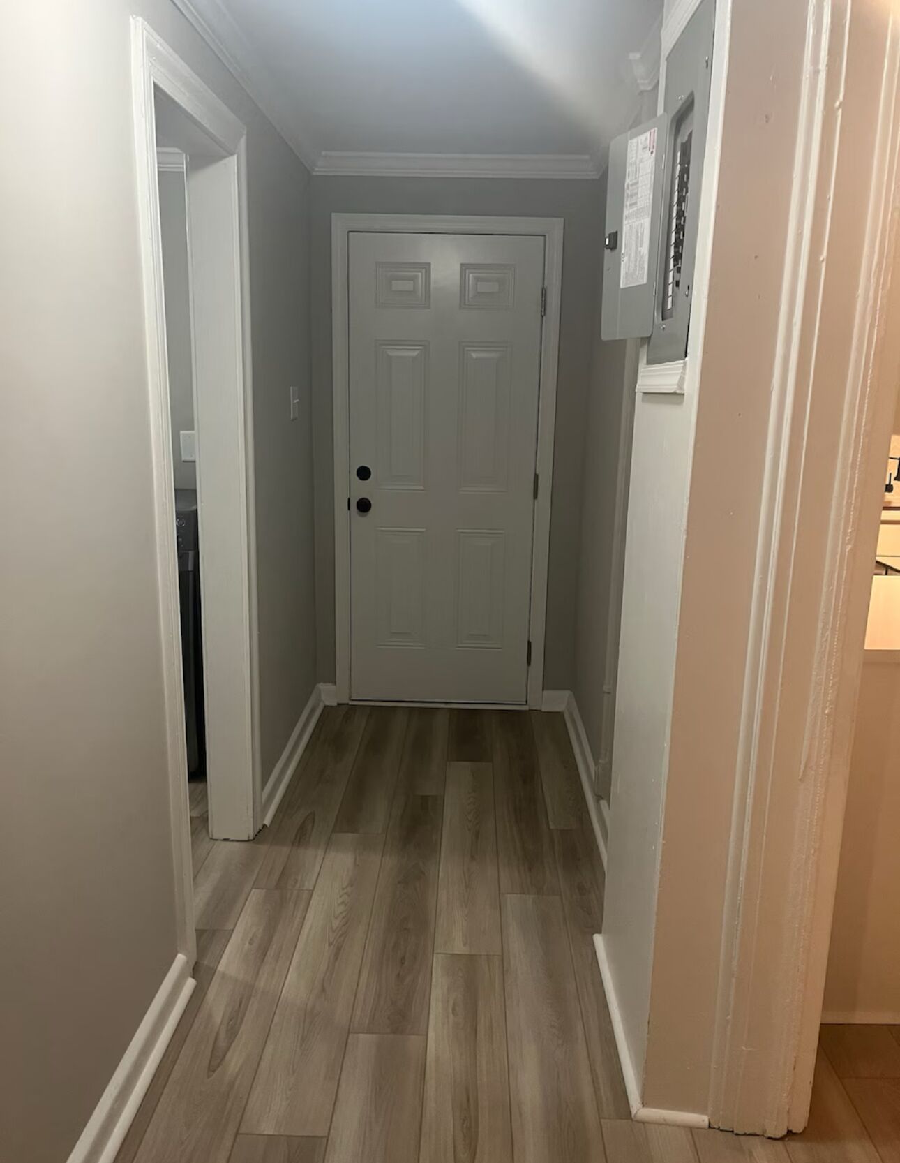 A narrow hallway with a wooden floor, a white door, and a light switch on the wall.