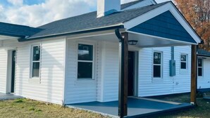 A single-story white house with a dark roof, a chimney, and a covered porch.