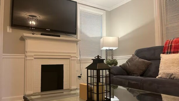 A living room with a flat-screen TV mounted above a fireplace, a glass coffee table with a lantern, and a sofa with cushions.