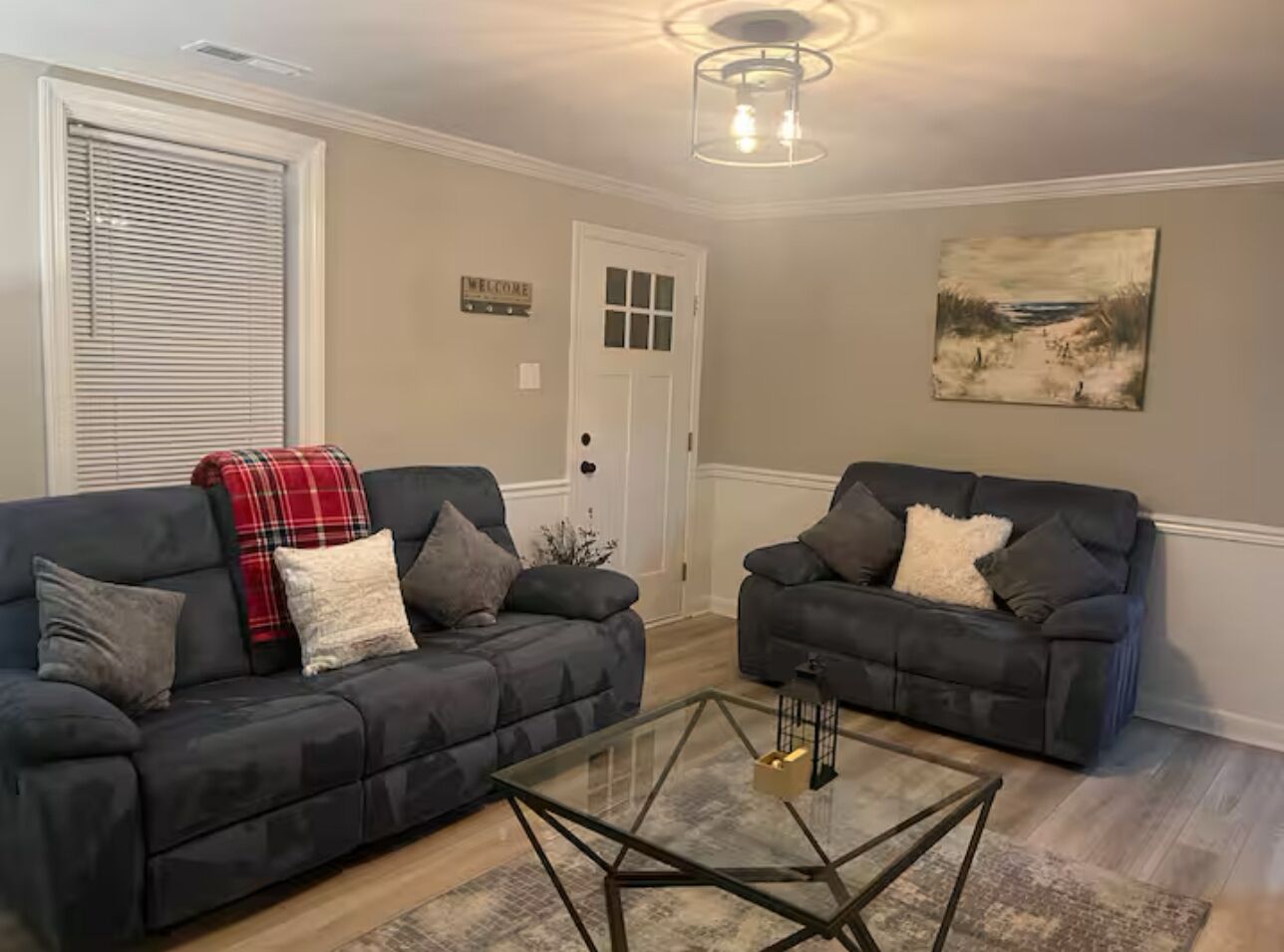 A living room with two dark sofas, a glass coffee table, a white door, and a painting on the wall.