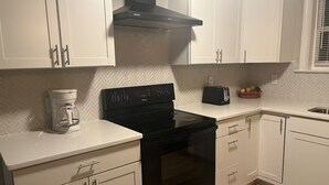 A kitchen with white cabinets, a black stove, and a coffee maker.