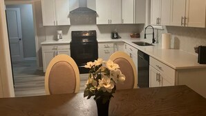 A modern kitchen with white cabinets, a black stove, and a dining area with a wooden table and chairs.