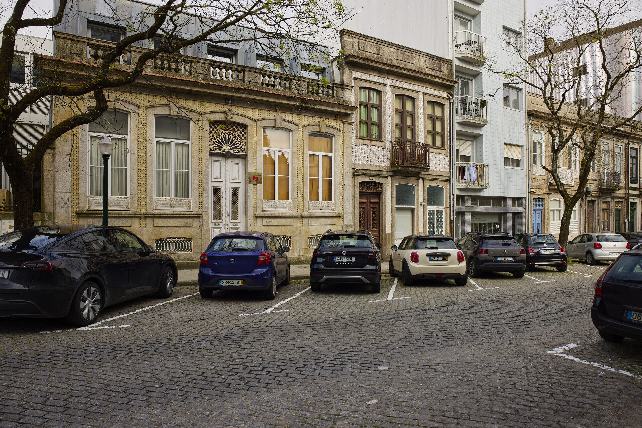 Una hilera de coches aparcados a lo largo de una calle adoquinada frente a un edificio con detalles arquitectónicos ornamentales.