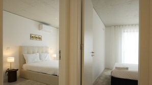 A hotel room with a bed, bedside table, lamp, air conditioning unit, and a window with curtains.