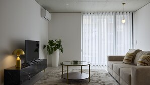 A modern living room with a TV, a round glass coffee table, a sofa, and a large plant.