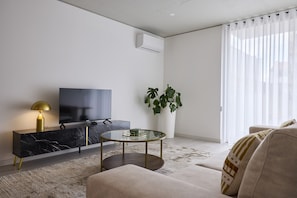 A modern living room with a TV, a glass coffee table, a sofa, a marble console, and a potted plant. - FLH Porto Central Apartment III (Oporto)