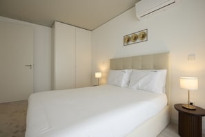 A hotel room with a large bed, two bedside lamps, a wall-mounted air conditioner, and a door. - FLH Porto Central Apartment III (Oporto)