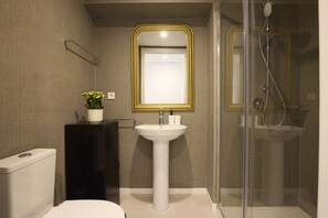 Un baño moderno con lavamanos pedestal, inodoro, cabina de ducha y espejo con marco dorado.