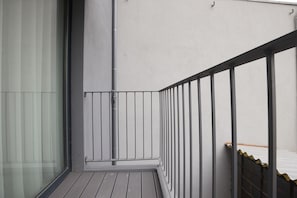 Ein Balkon mit Metallgeländer, einer Glastür und einer weißen Wand.