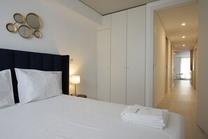 A hotel room with a bed, a nightstand, a lamp, a wardrobe, and a hallway.