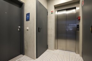An elevator with a metallic finish, a fire alarm button, and a checkered floor pattern.