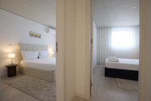 Ein Hotelzimmer mit zwei Betten, einem Nachttisch mit Lampe, einer Wandleuchte und einem Fenster mit durchsichtigen Vorhängen.