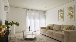 A modern living room with a beige sofa, a round coffee table, a potted plant, and a large window with sheer curtains. - FLH Porto Central Apartment I (Oporto)
