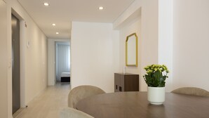 A hotel room with a wooden dining table, beige chairs, a white vase with flowers, a wooden cabinet, and a mirror on the wall. - FLH Porto Central Apartment I (Oporto)