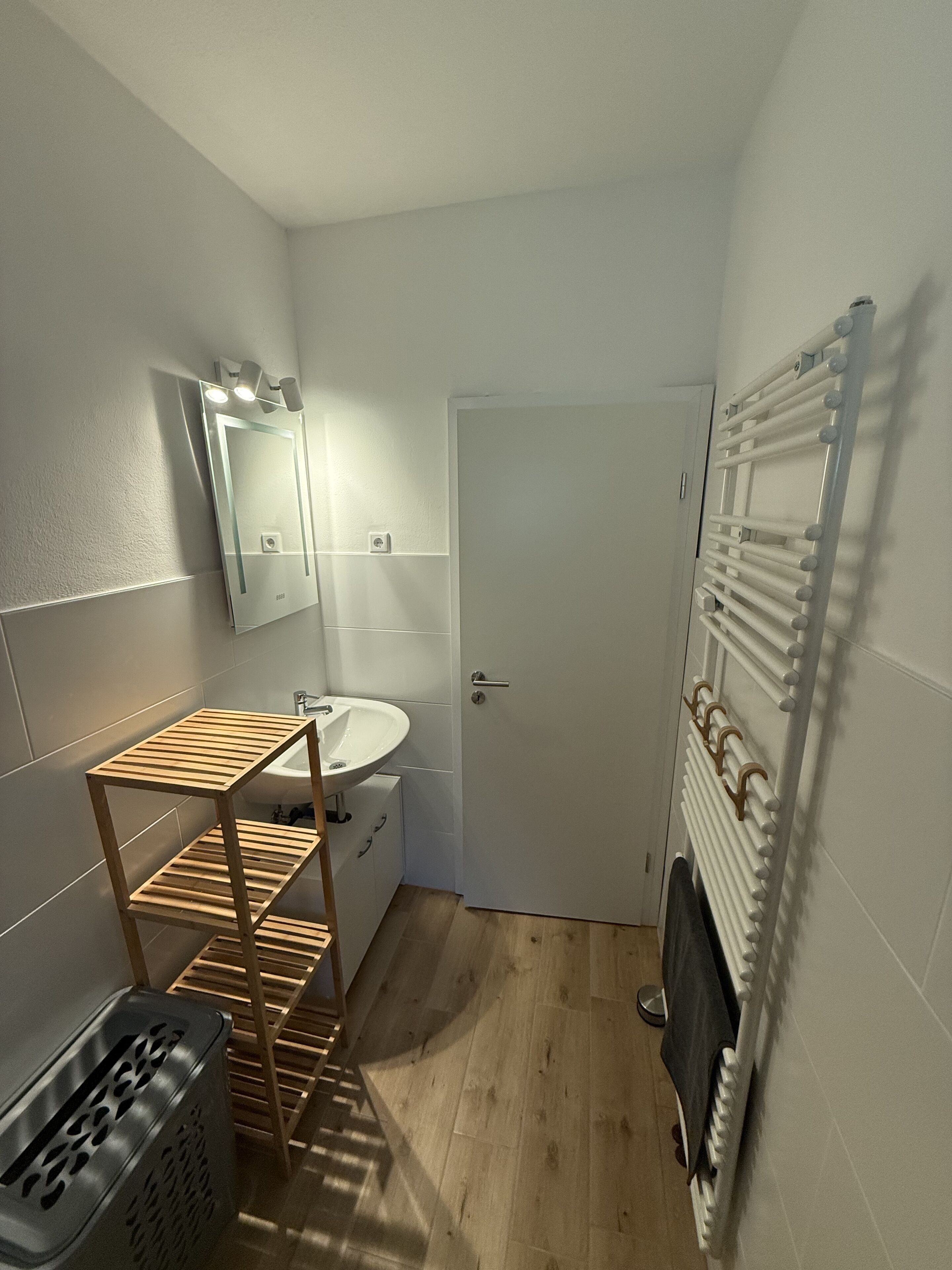 A small bathroom with a wooden shelf, a sink, a mirror, and a radiator.