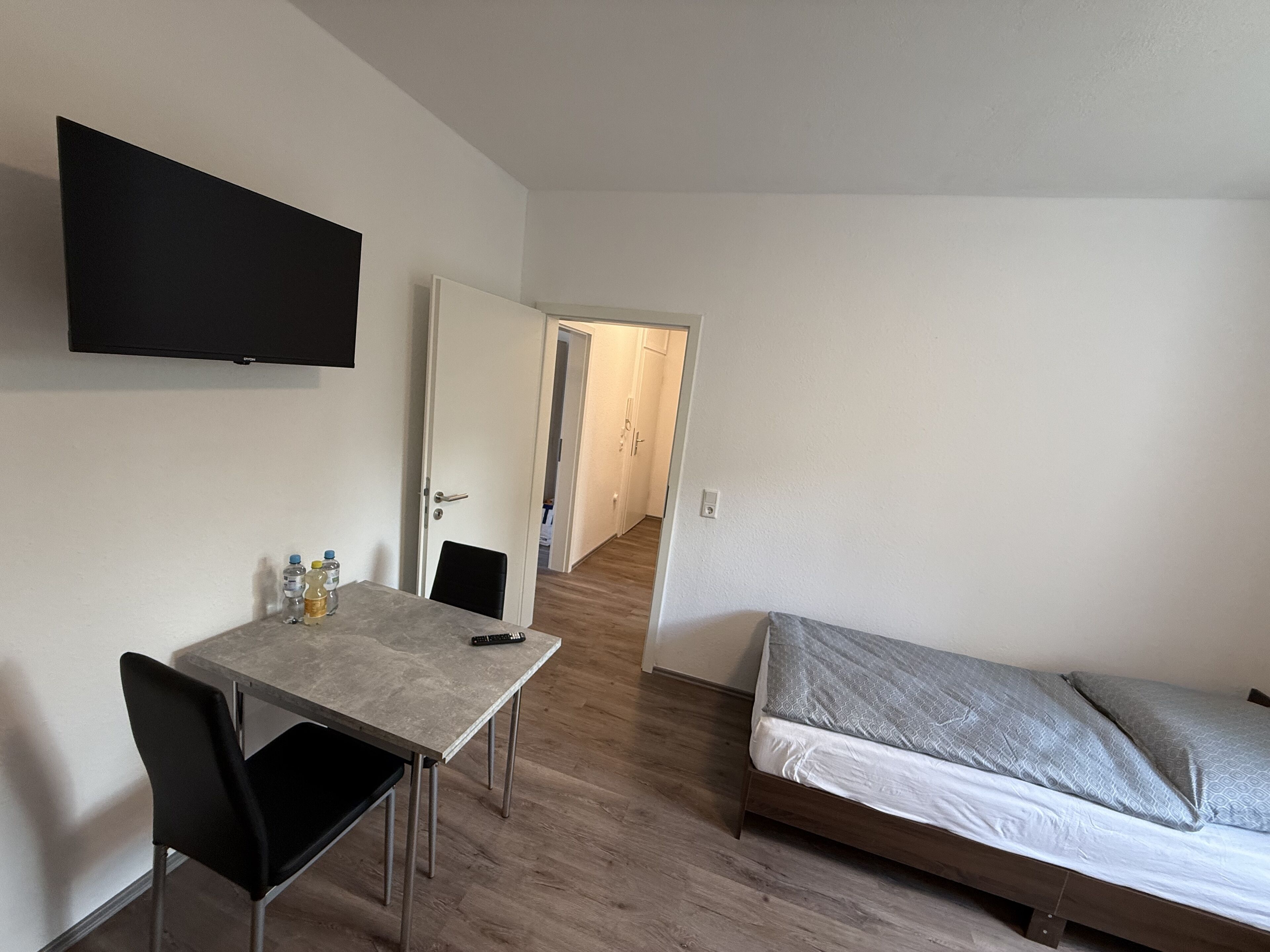 Ein schlichter, einfach eingerichteter Raum mit einem Bett, einem Schreibtisch und einem Fernseher.
