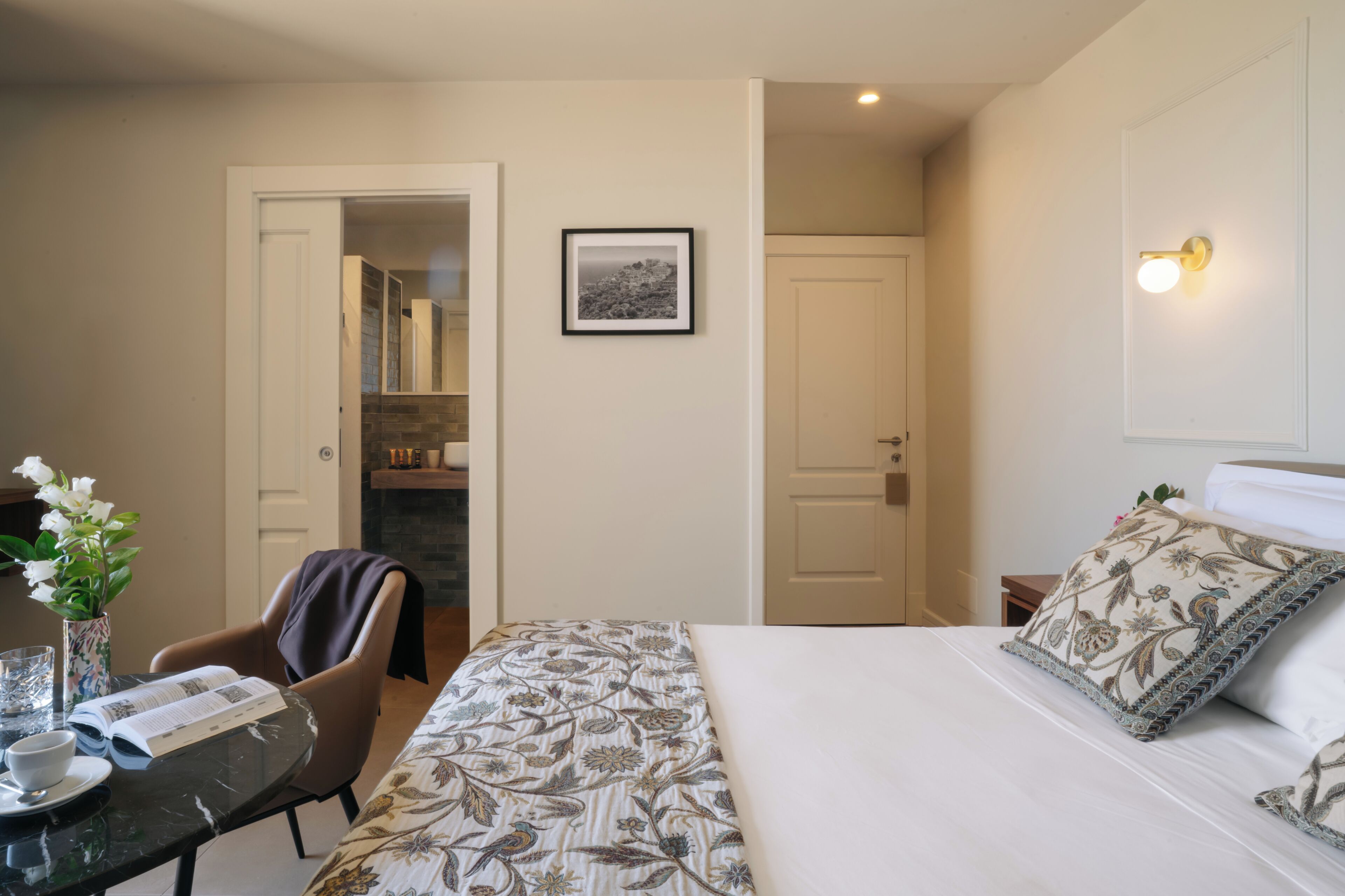 Een hotelkamer met een bed, een bureau met een bloevas, een stoel en een lijst aan de muur.