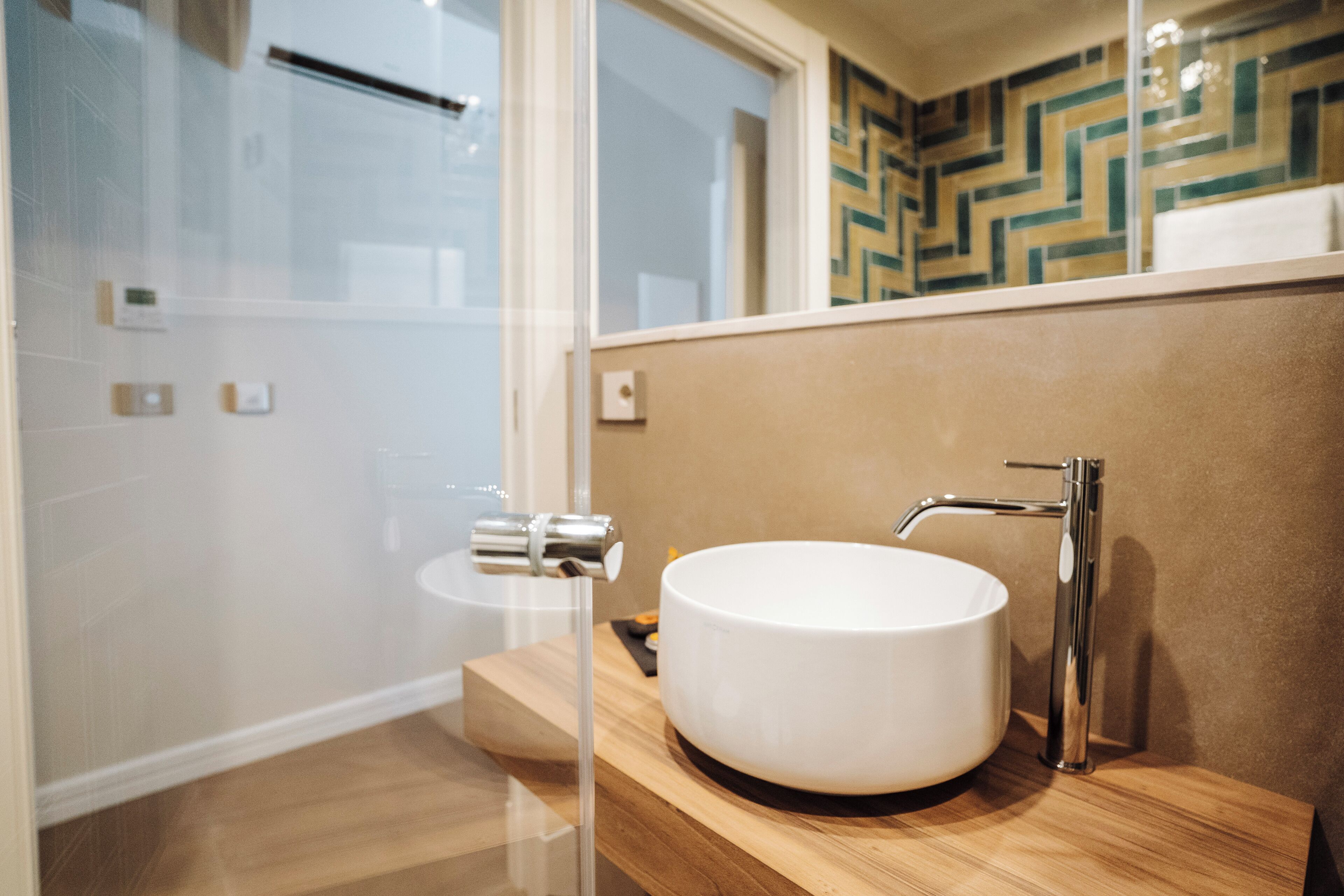 A modern bathroom with a round white sink, a wooden vanity, and a glass shower enclosure.