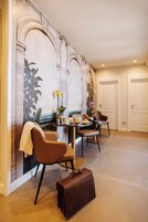 Un comedor con una mesa preparada para dos personas, un maletín de cuero marrón en el suelo y un mural con detalles arquitectónicos en la pared.