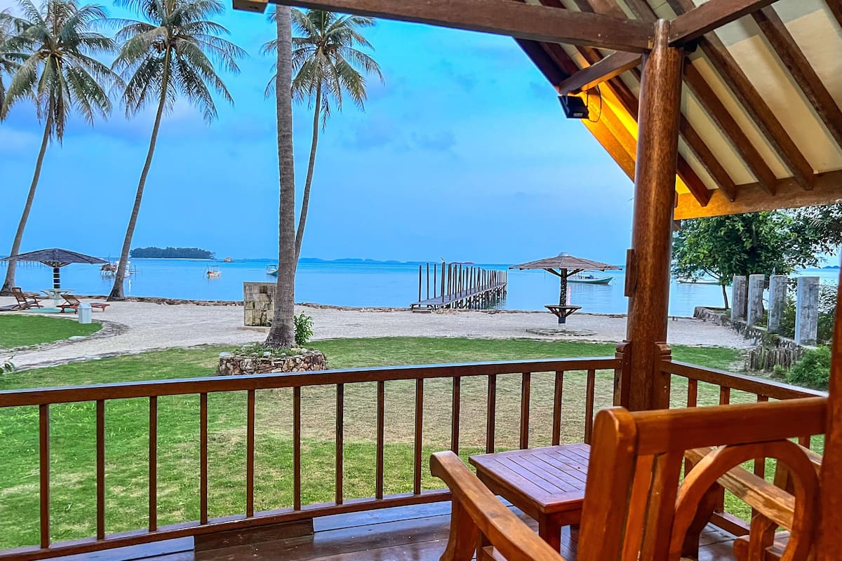 Una terraza de madera con vistas a una playa, palmeras y un muelle.