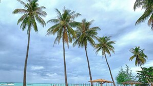 A beach with palm trees, a sandy shore, and a wooden pier. - Arys Lagoon Resort Karimunjawa (Karimunjawa)