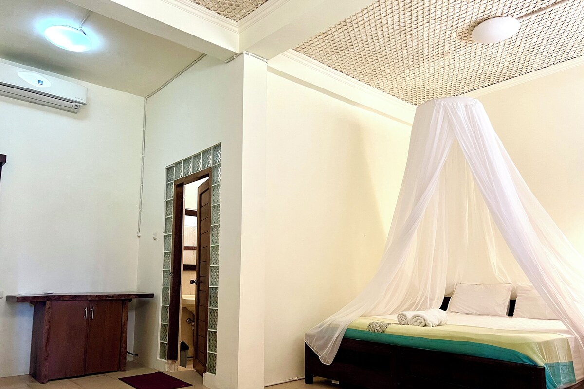 A bedroom with a bed under a canopy, a wooden cabinet, and a tiled floor.