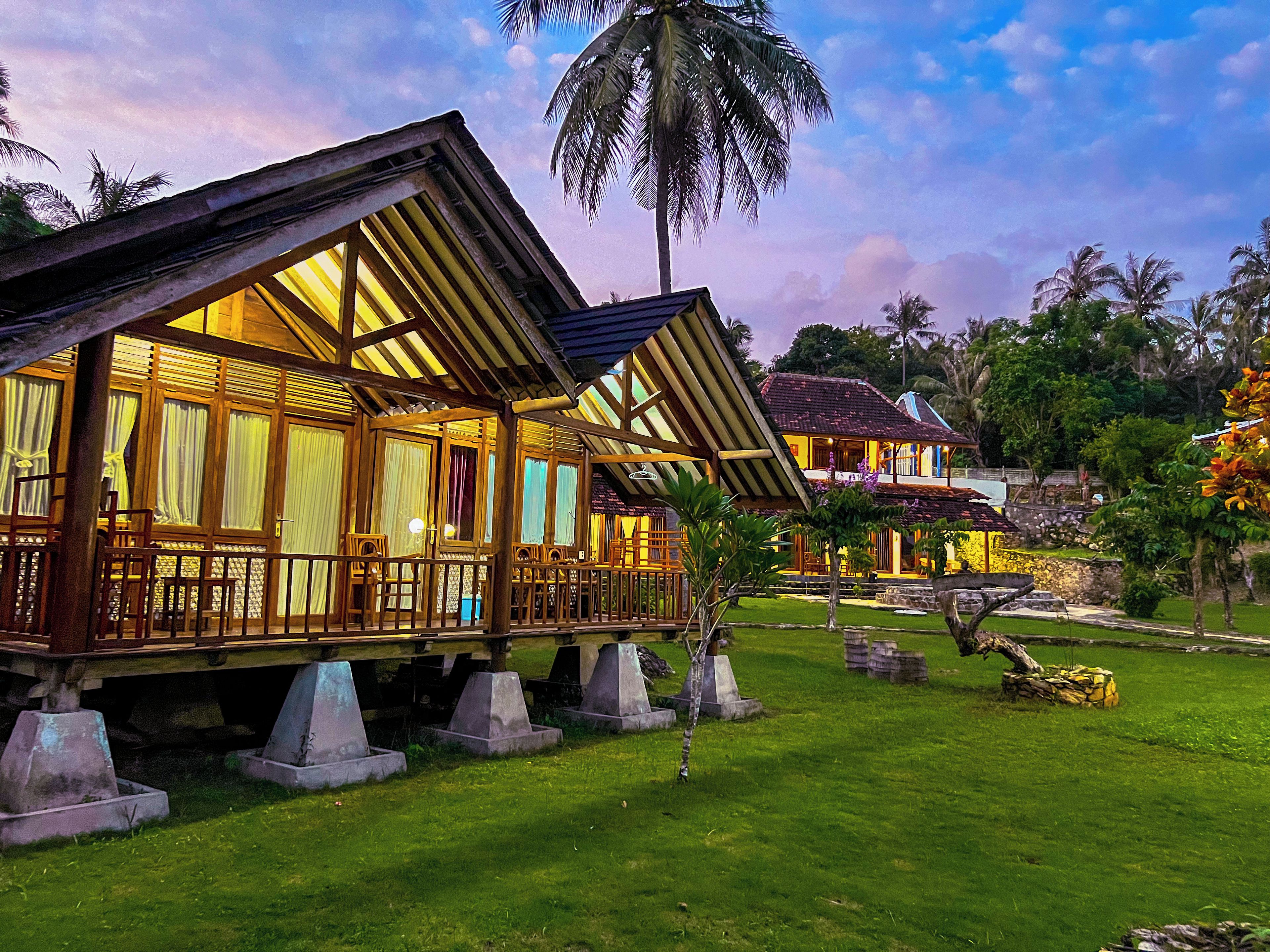 A wooden house with a balcony, surrounded by a well-maintained lawn and palm trees.