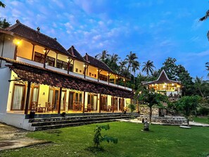A two-story building with a balcony, a covered outdoor seating area, and a stone structure in the background. - Arys Lagoon Resort Karimunjawa (Karimunjawa)