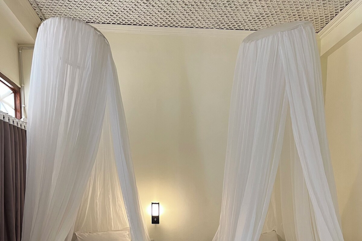 Two beds with canopy beds, a nightstand, and a wall-mounted light fixture.