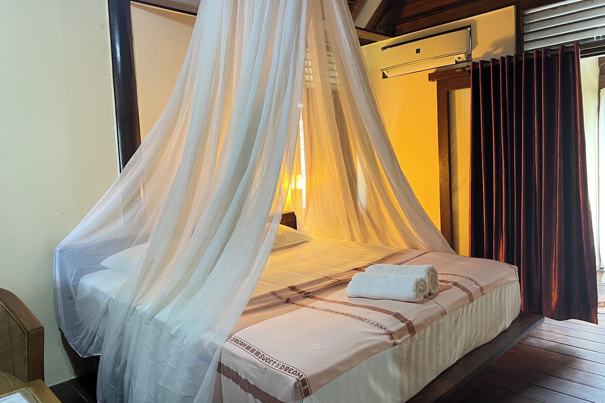 A bed with a canopy, a bedside table, and a wall-mounted air conditioning unit.