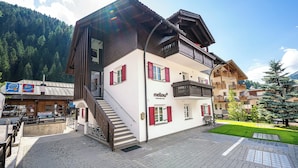Un edificio de dos pisos con fachada de madera, contraventanas rojas y un balcón.
