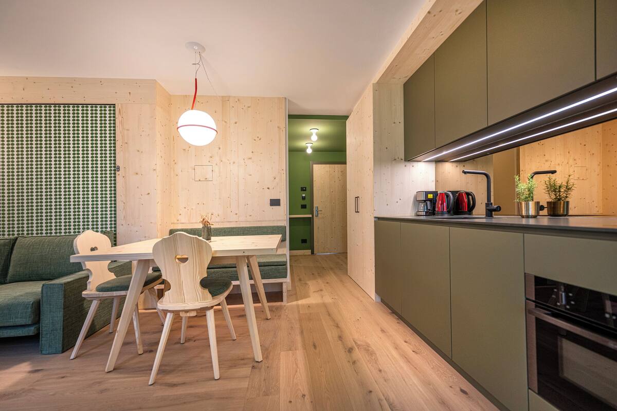 Une cuisine moderne avec des meubles en bois, une table à manger avec des chaises et un canapé vert.