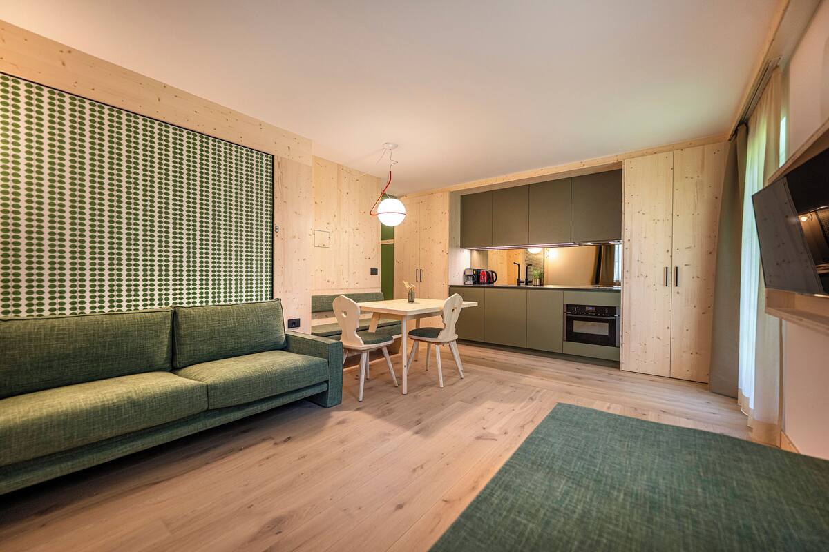 Une cuisine moderne avec des meubles en bois, un coin repas avec un canapé vert et des chaises blanches, et une petite table.