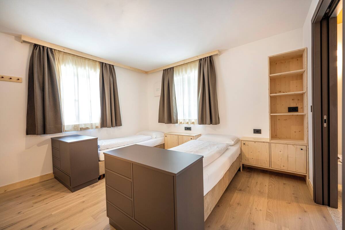 Une chambre moderne avec deux lits, une armoire en bois et une étagère intégrée.