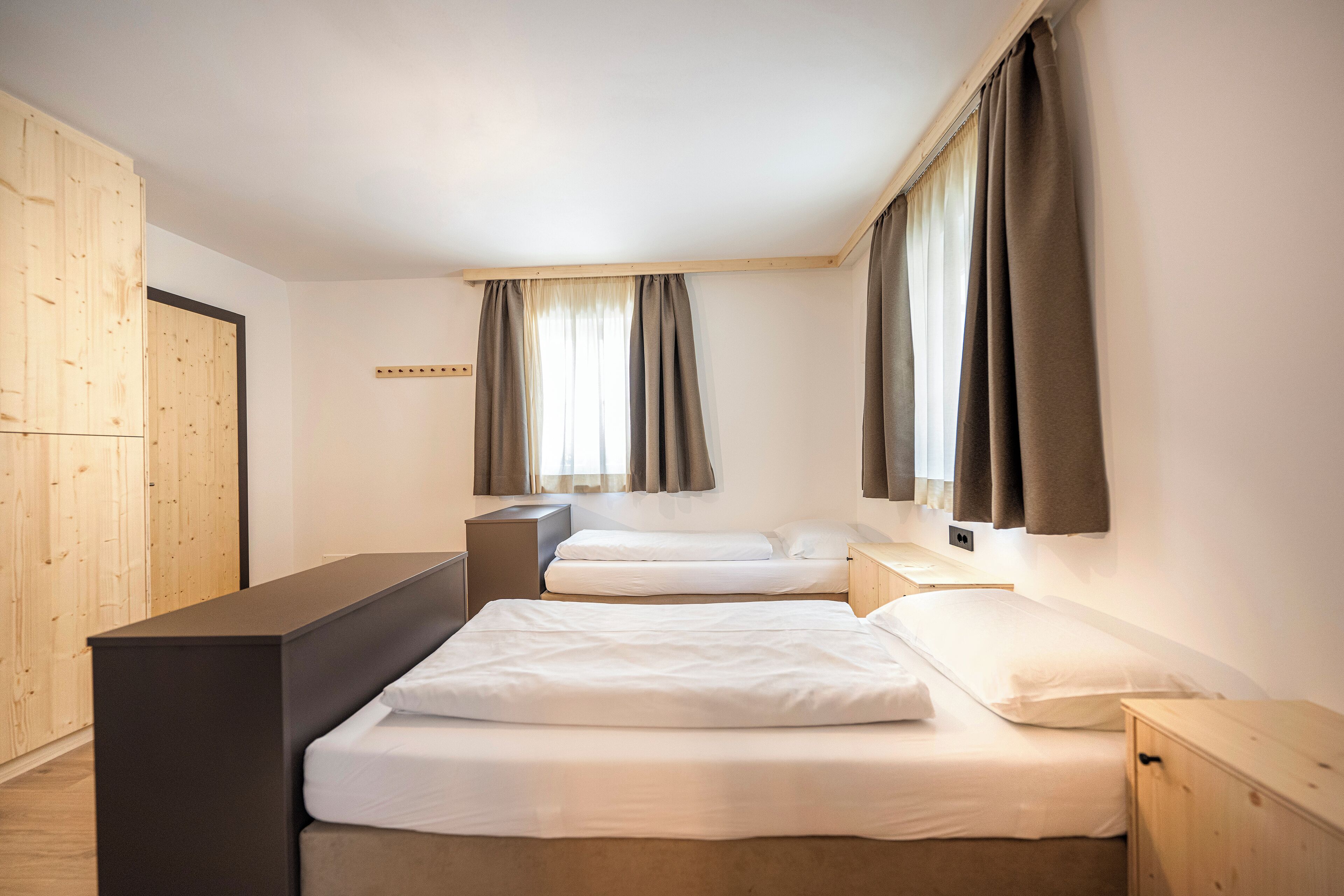 A modern hotel room with a large bed, a desk, and a wardrobe.