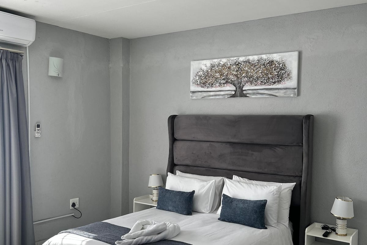 Une chambre moderne avec un grand lit, une tête de lit, des tables de chevet, une œuvre d’art accrochée au mur et une fenêtre avec des rideaux.