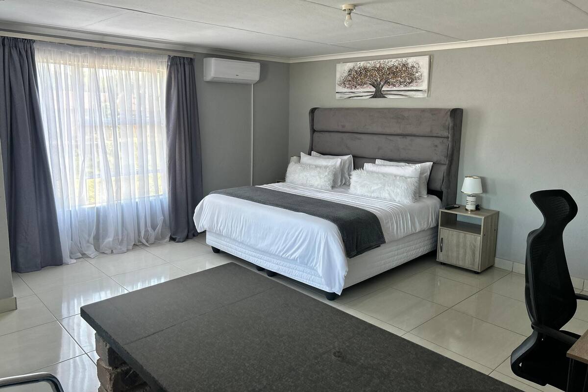 Une chambre moderne avec un grand lit, une table de chevet avec une lampe, une chaise et un tableau au mur.