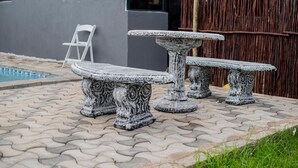 A stone outdoor seating area with a pool in the background. - Silalise Lodge (Greater Tubatse)