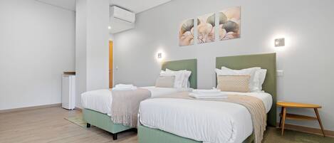 A modern hotel room with two beds, a small table, and a wall-mounted air conditioner.