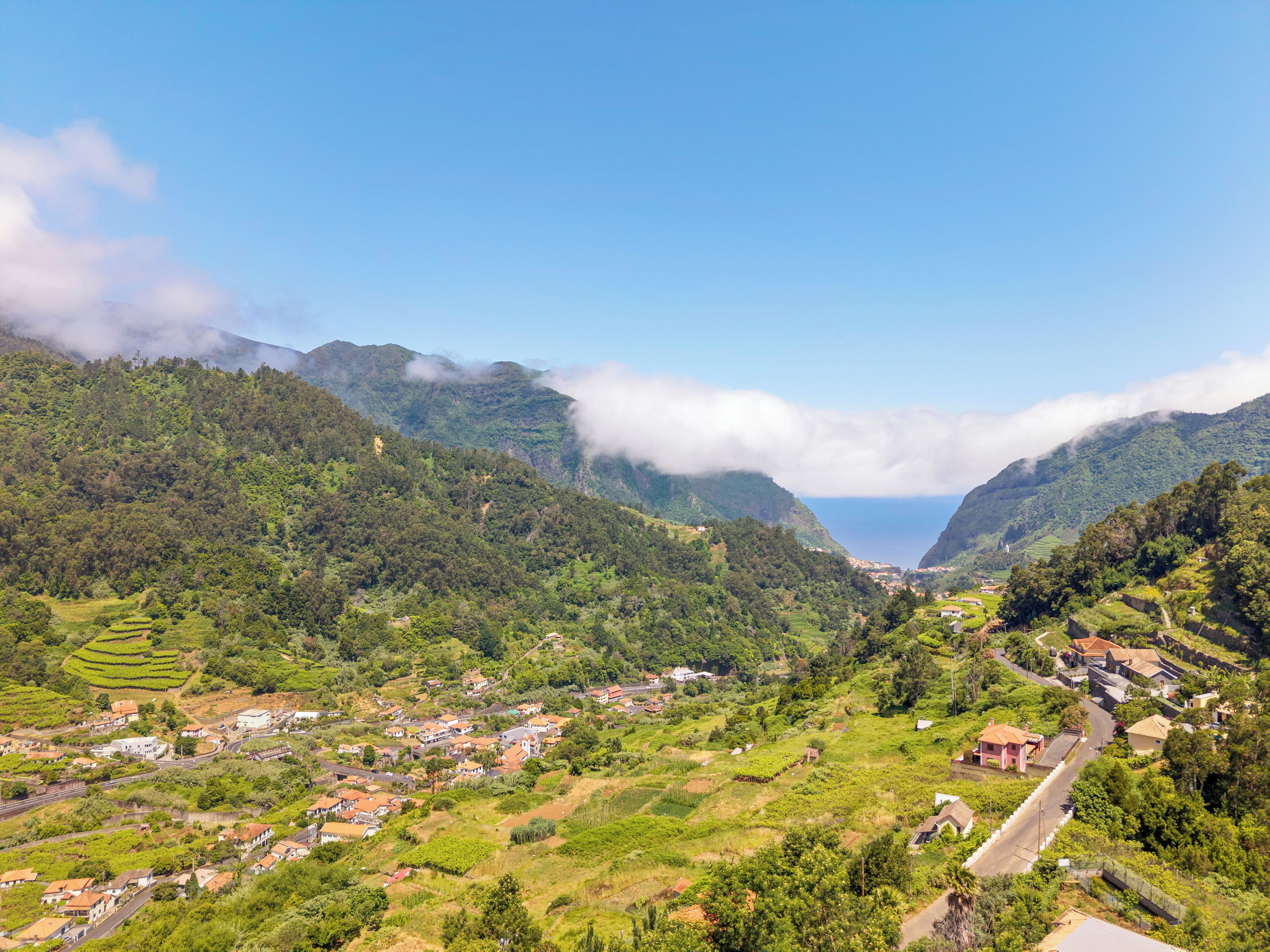 Un paysage montagneux avec des champs en terrasses, un petit village et une vue dégagée sur l’océan.
