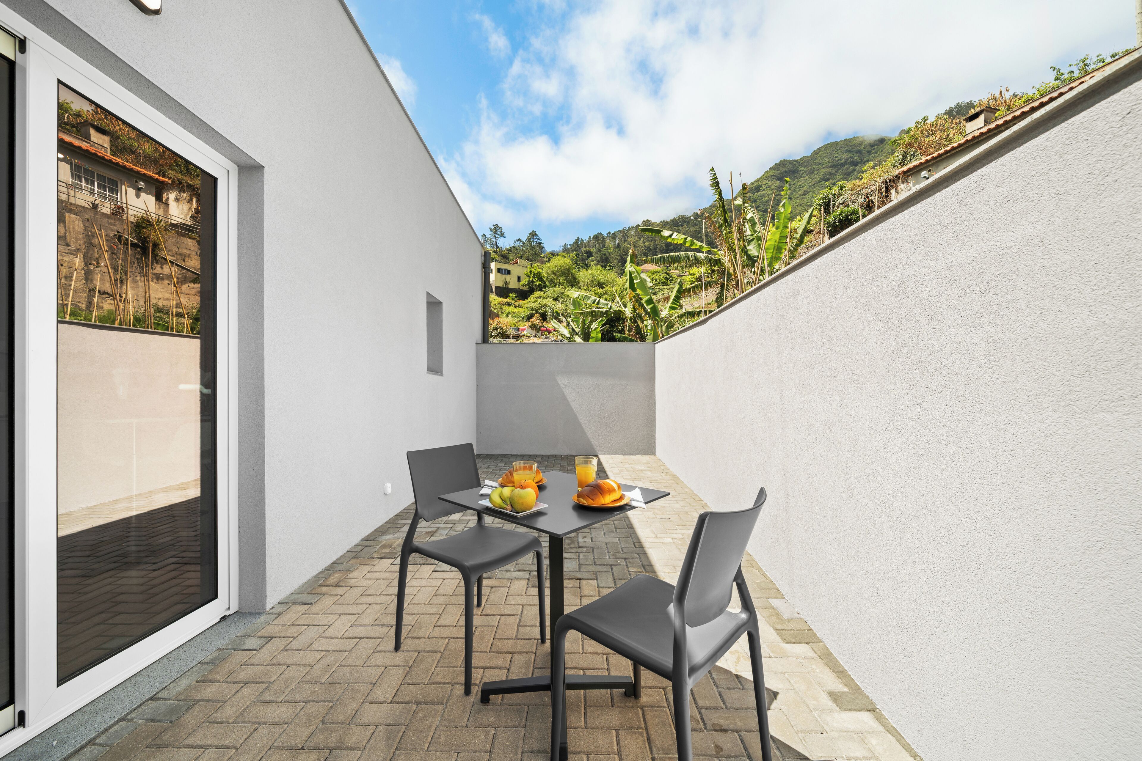 A patio with a table set for two, a glass of orange juice, and a plate of fruit.