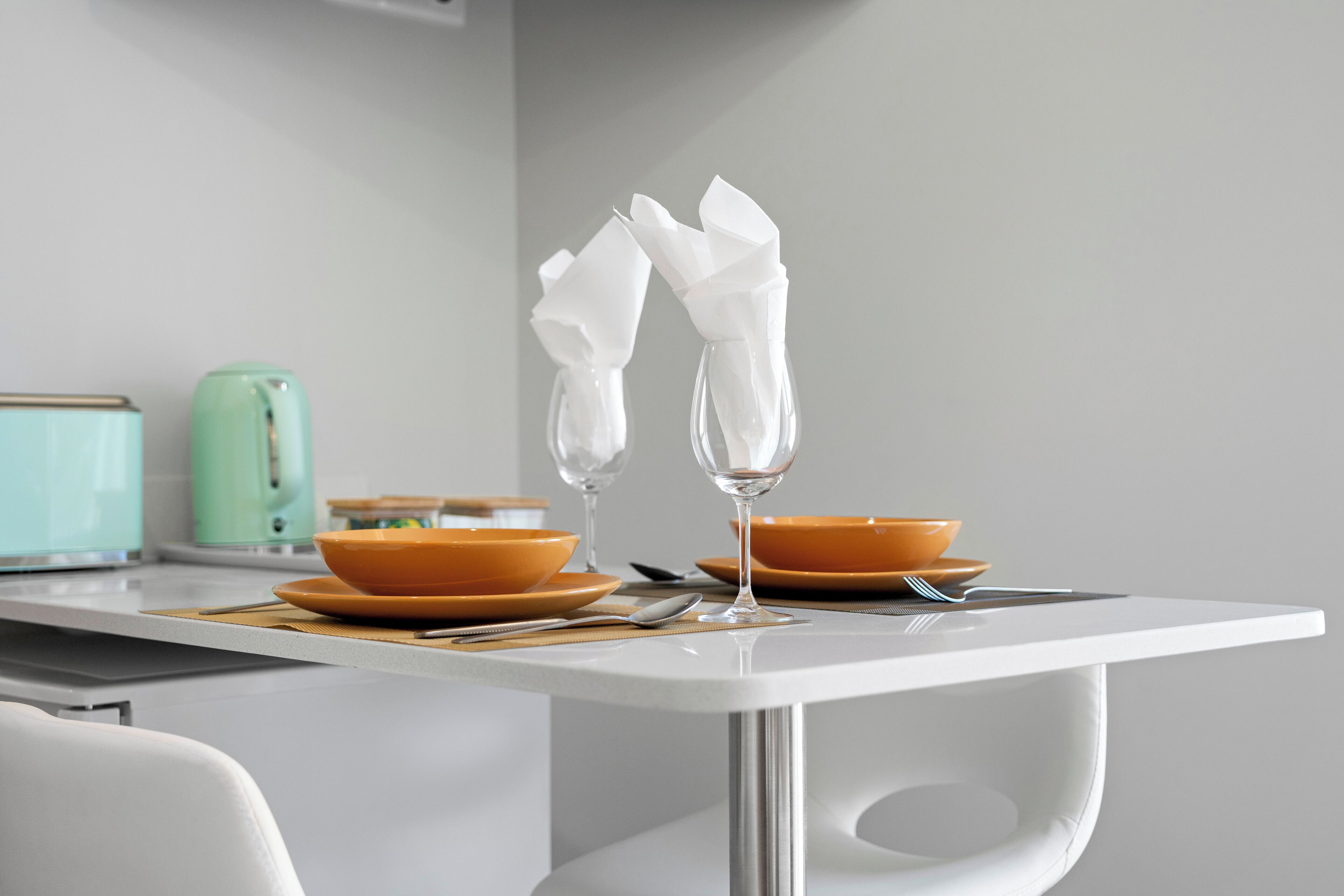 Una mesa de comedor moderna con dos cuencos naranjas, un vaso transparente y una servilleta blanca.