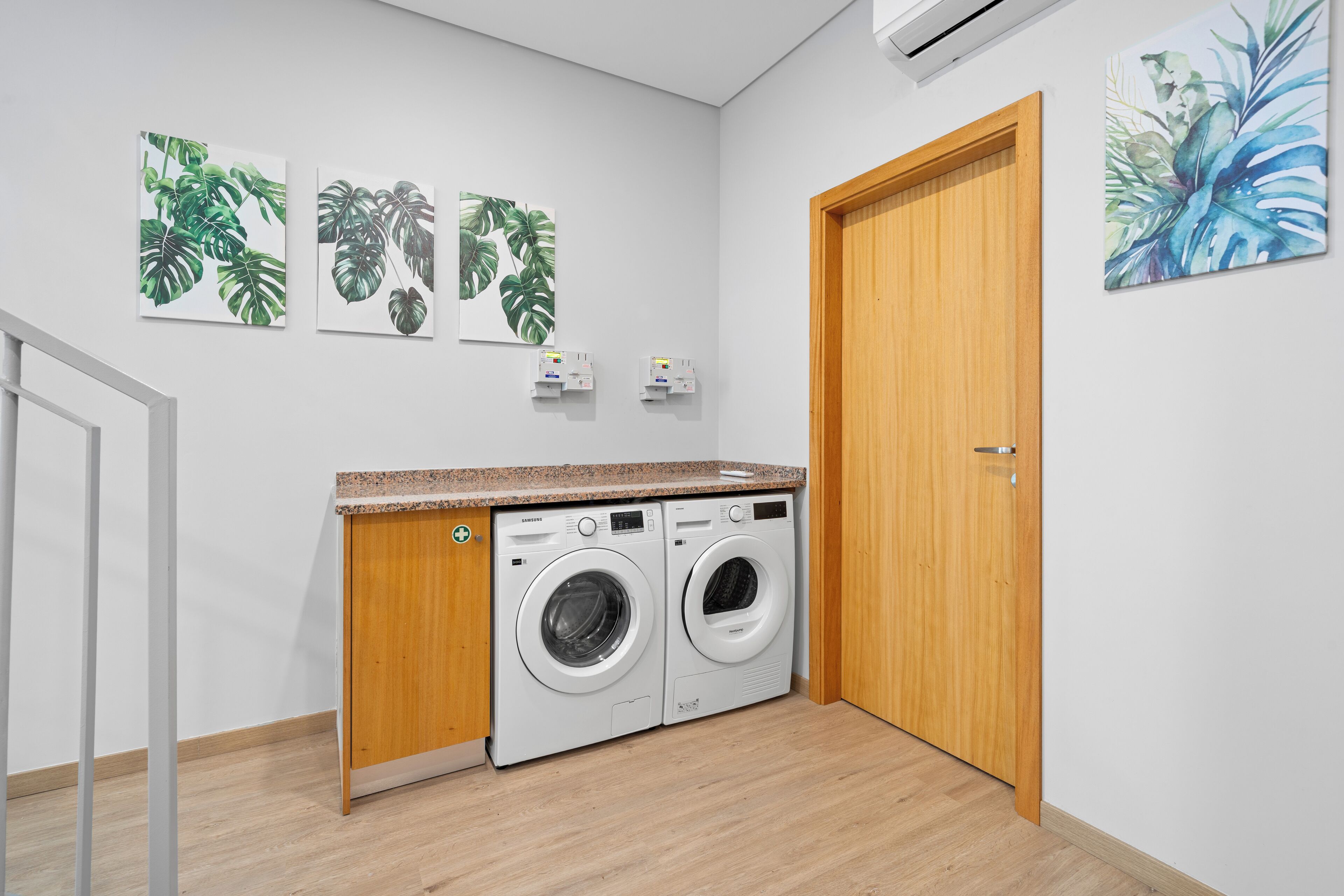 A laundry room with two washing machines, wooden cabinets, and three wall-mounted artwork pieces.