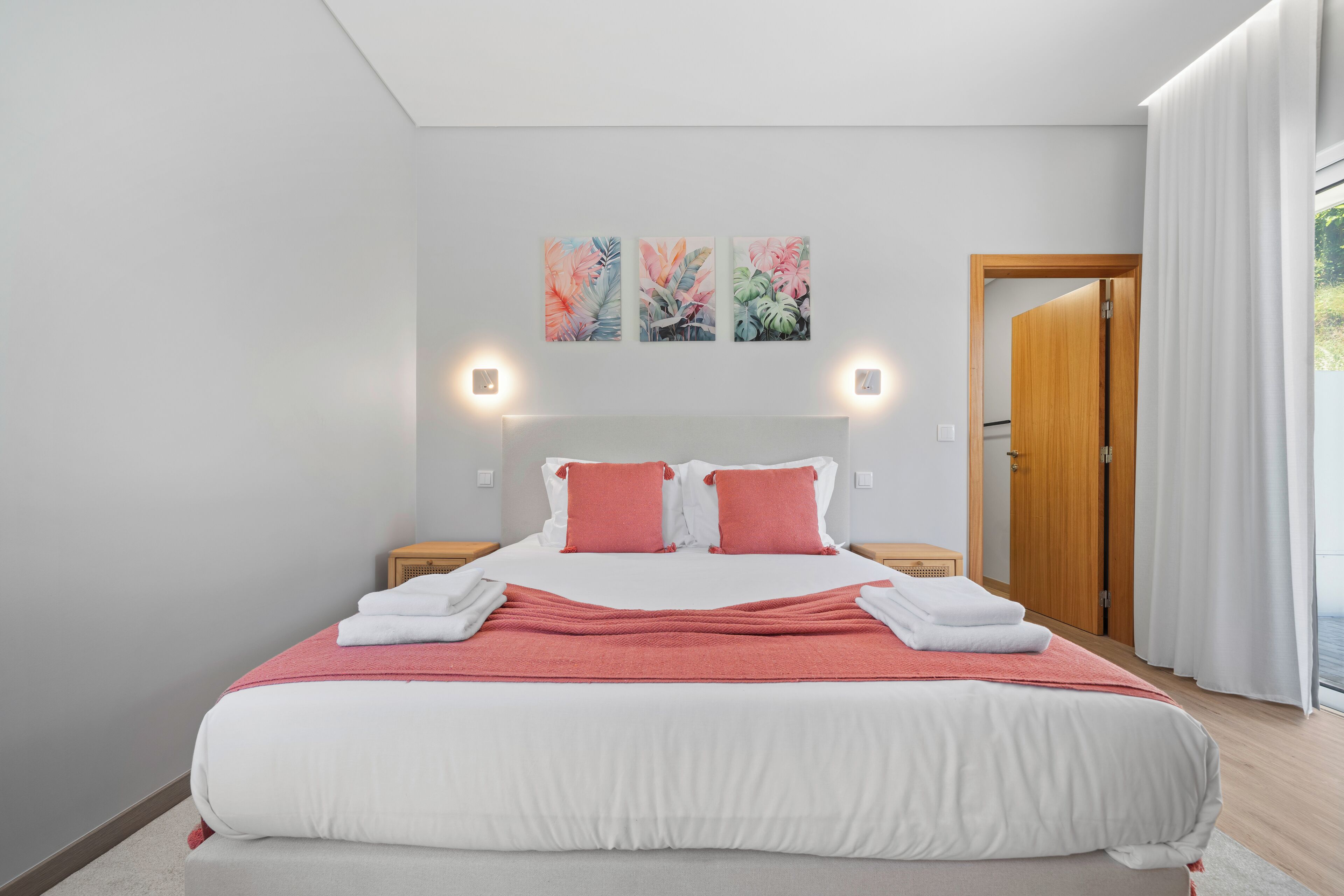 A neatly made bed with white and pink bedding, a wooden headboard, and two wall-mounted lights.
