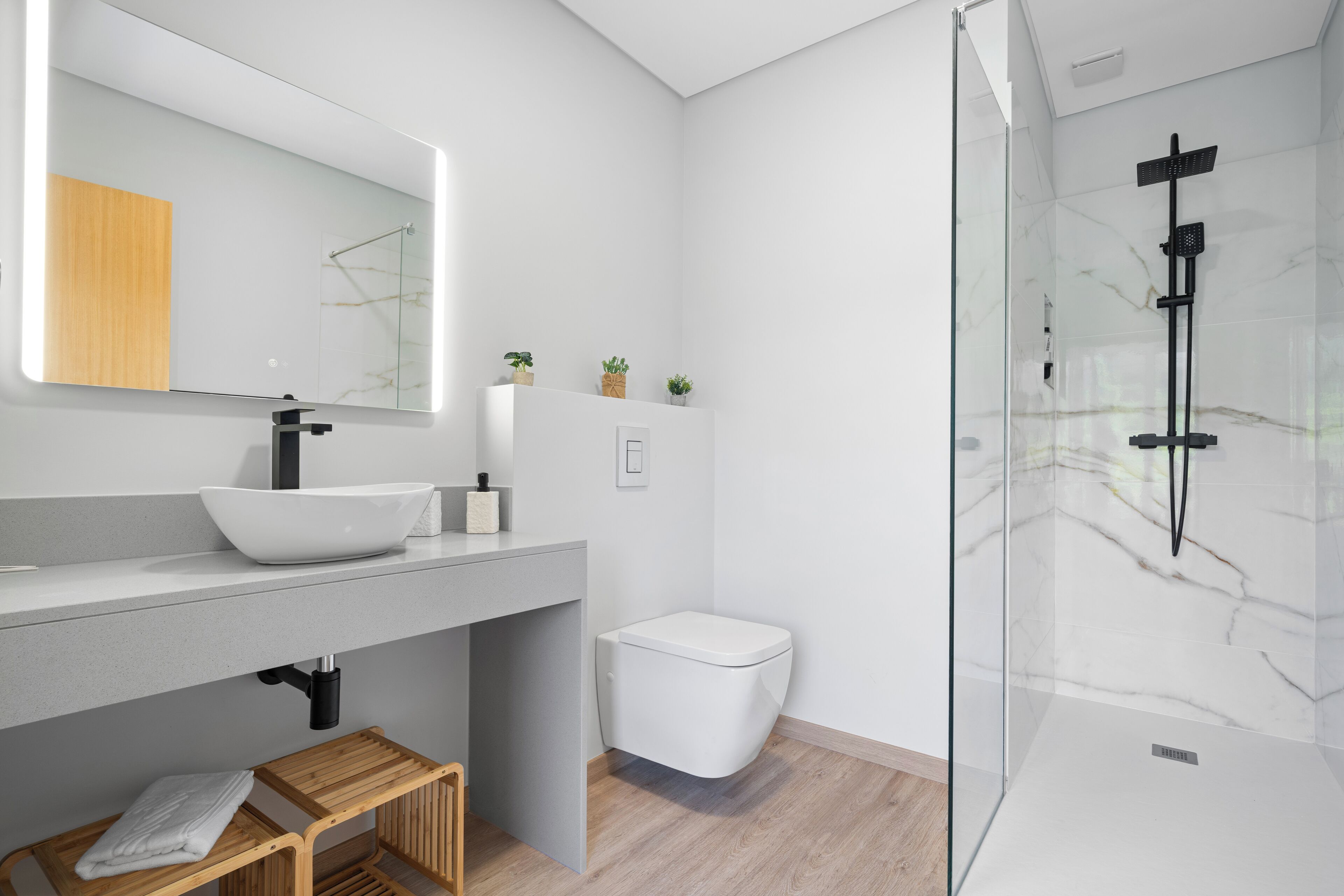 Un baño moderno con lavamanos blanco, espejo y cabina de ducha de vidrio.
