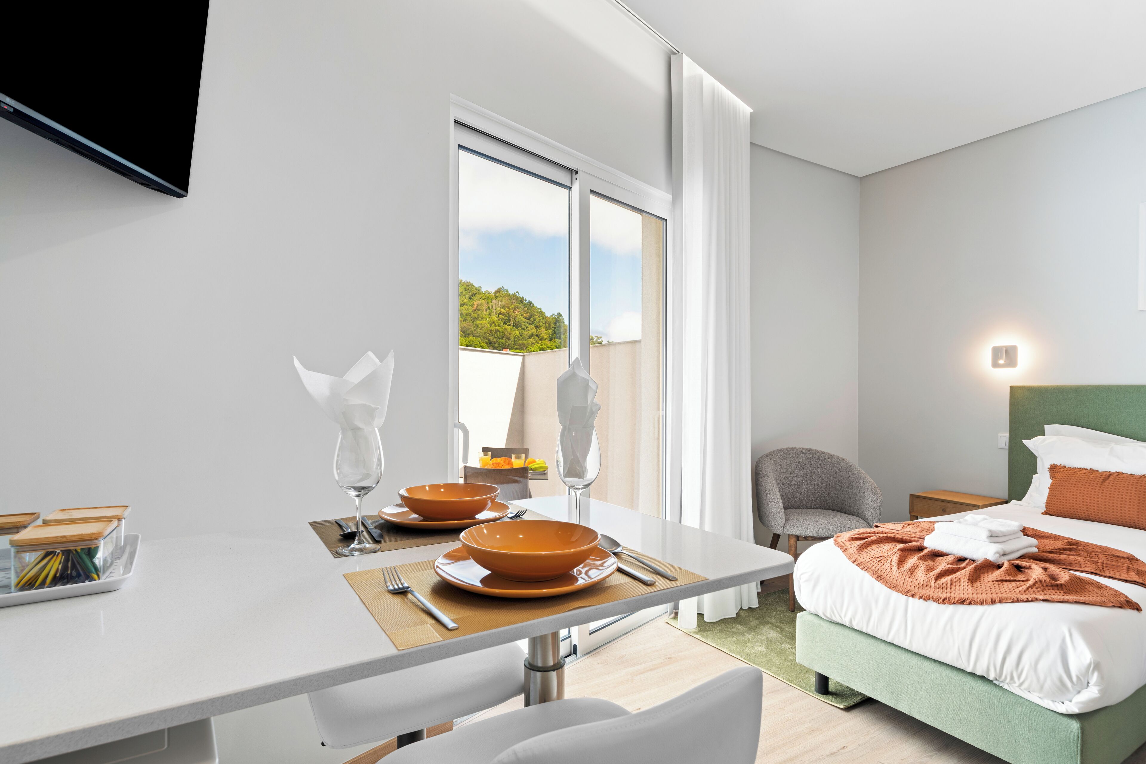 Una habitación de hotel moderna con cama, mesita de noche y zona de comedor con mesa para dos.
