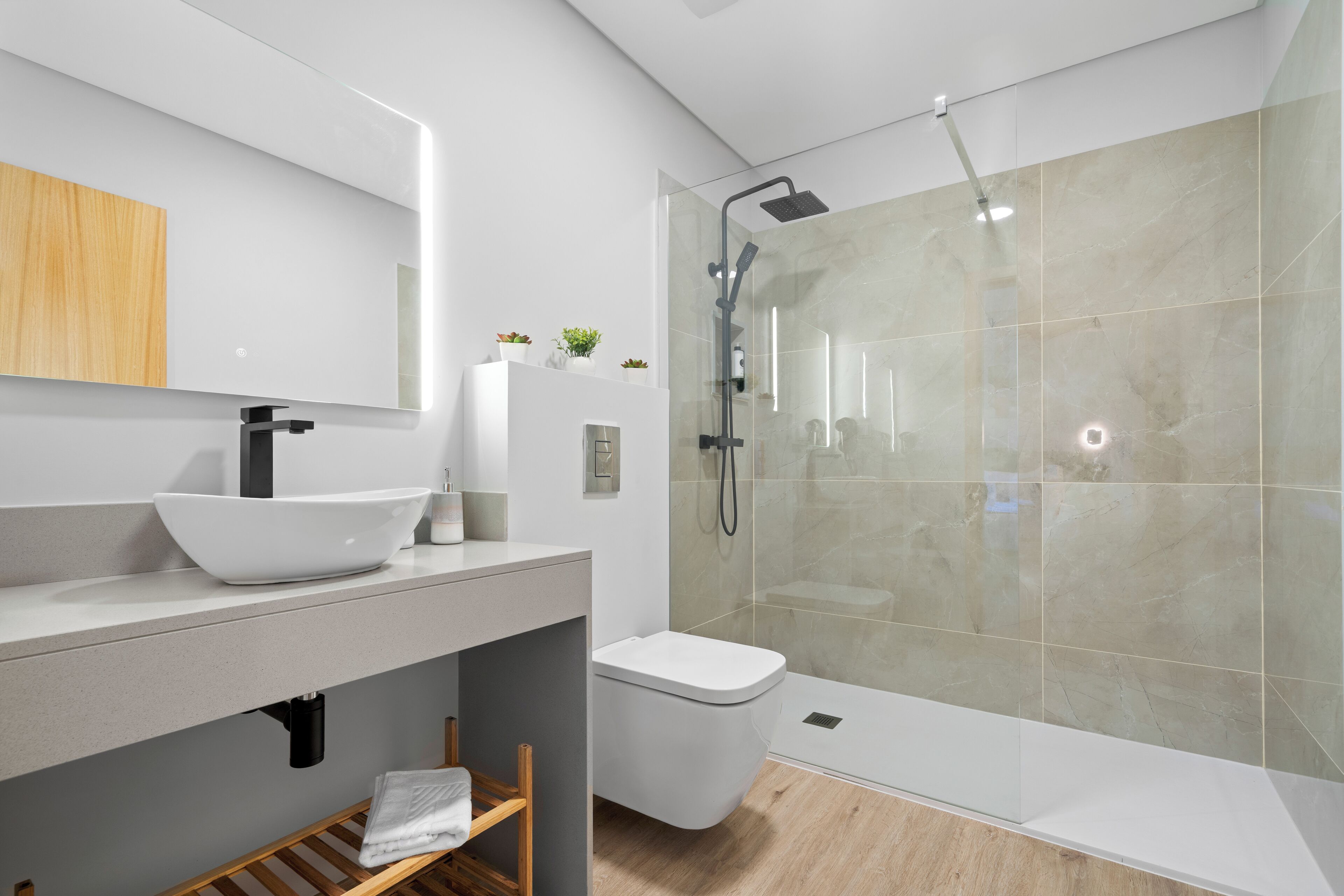 Une salle de bain moderne avec un lavabo blanc, une douche à parois de verre et une étagère en bois.