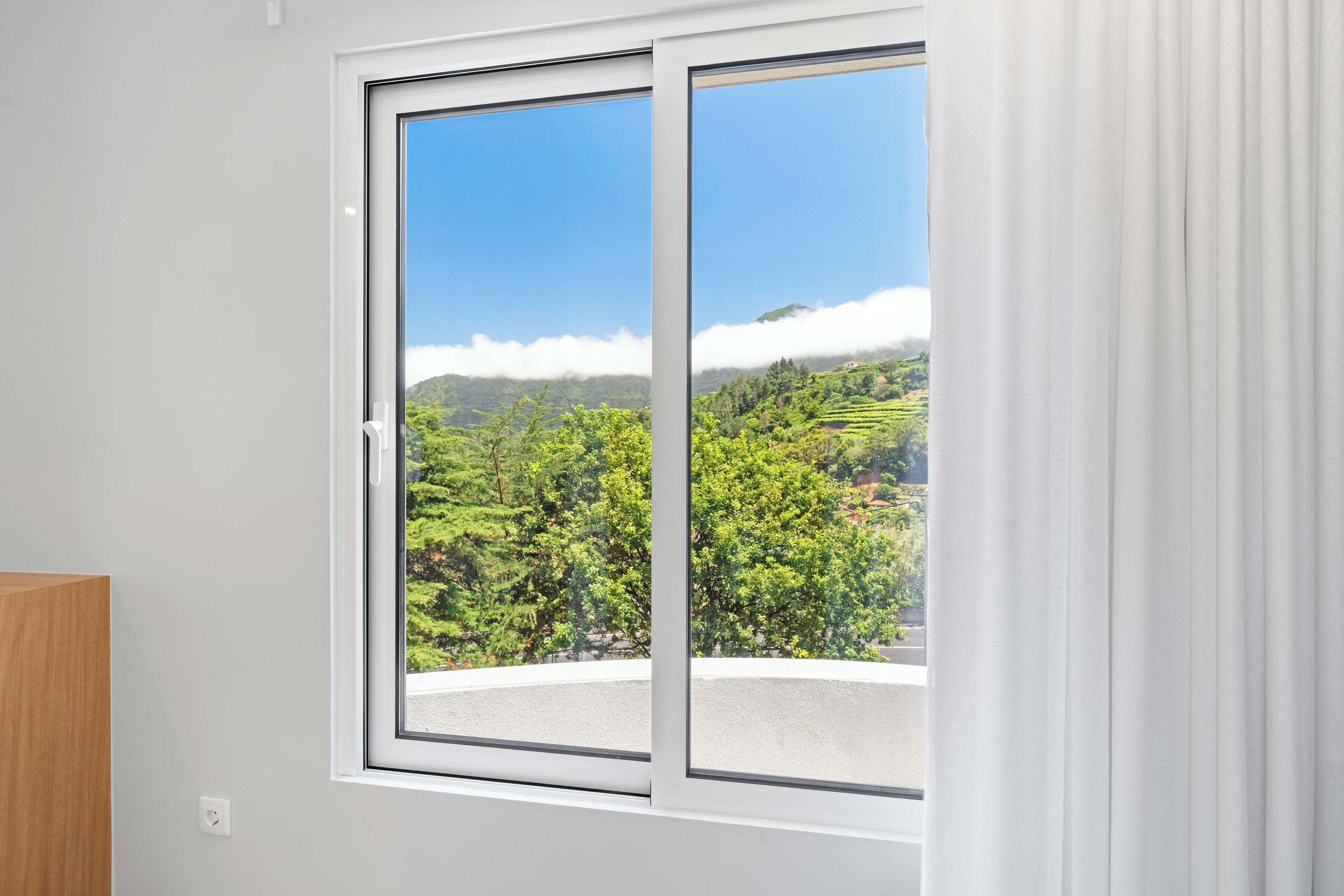 A room with a large sliding glass door leading to a scenic view of green hills and a clear blue sky.