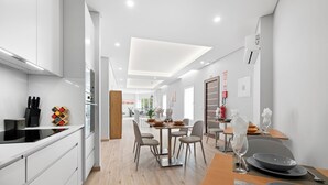 Una cocina moderna con muebles blancos, un comedor con mesa y sillas de madera, y un extintor a la vista en la pared.