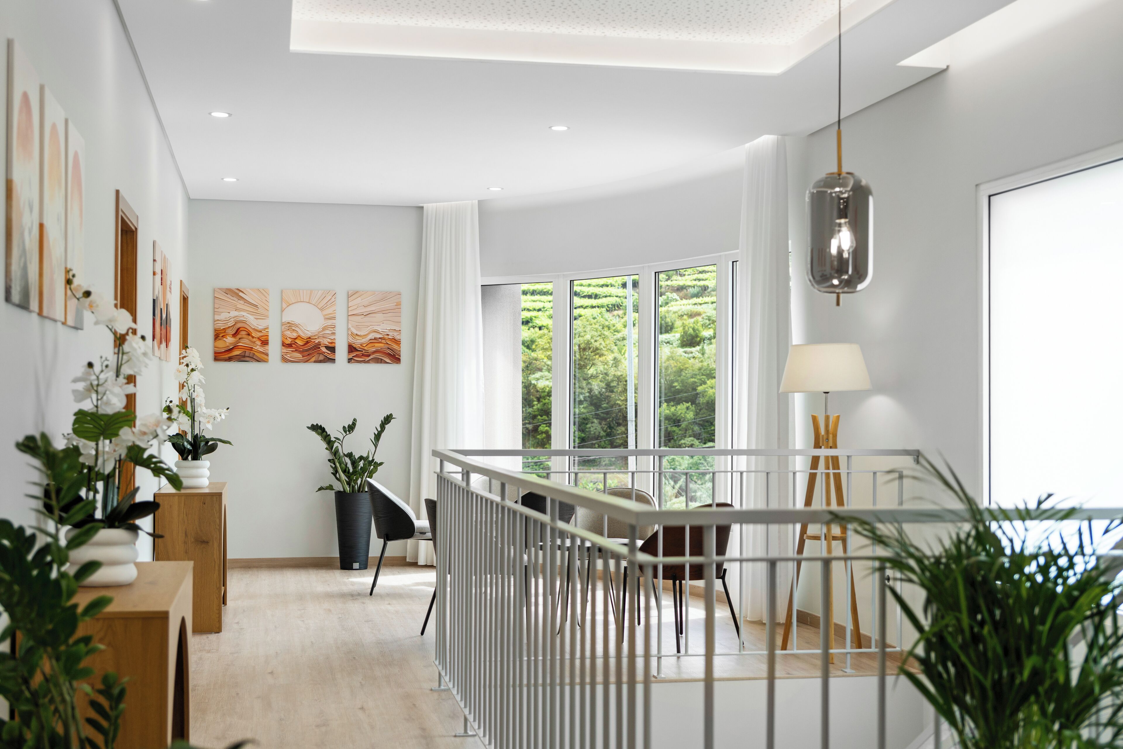 A modern interior with a wooden floor, a dining area with a white railing, and large windows offering a view of greenery.